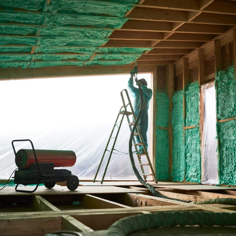 Worker spraying polyurethane foam for insulating wooden frame house.